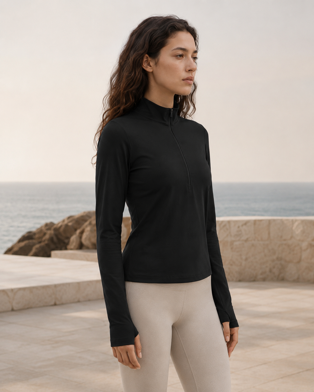 Woman wearing the NORTHE Studio Form Jacket in Black with neutral leggings, shown from the side in a coastal lifestyle setting.