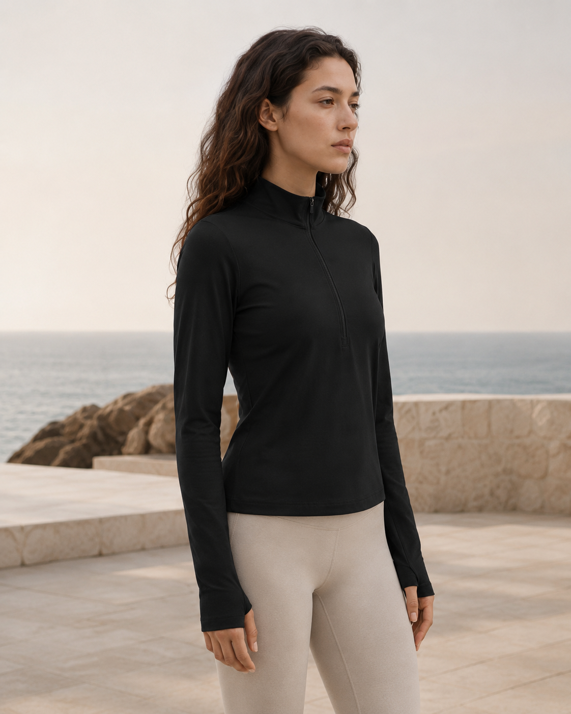 Woman wearing the NORTHE Studio Form Jacket in Black with neutral leggings, shown from the side in a coastal lifestyle setting.