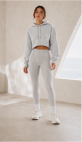 Person wearing a gray hoodie and leggings set in a minimalistic room.