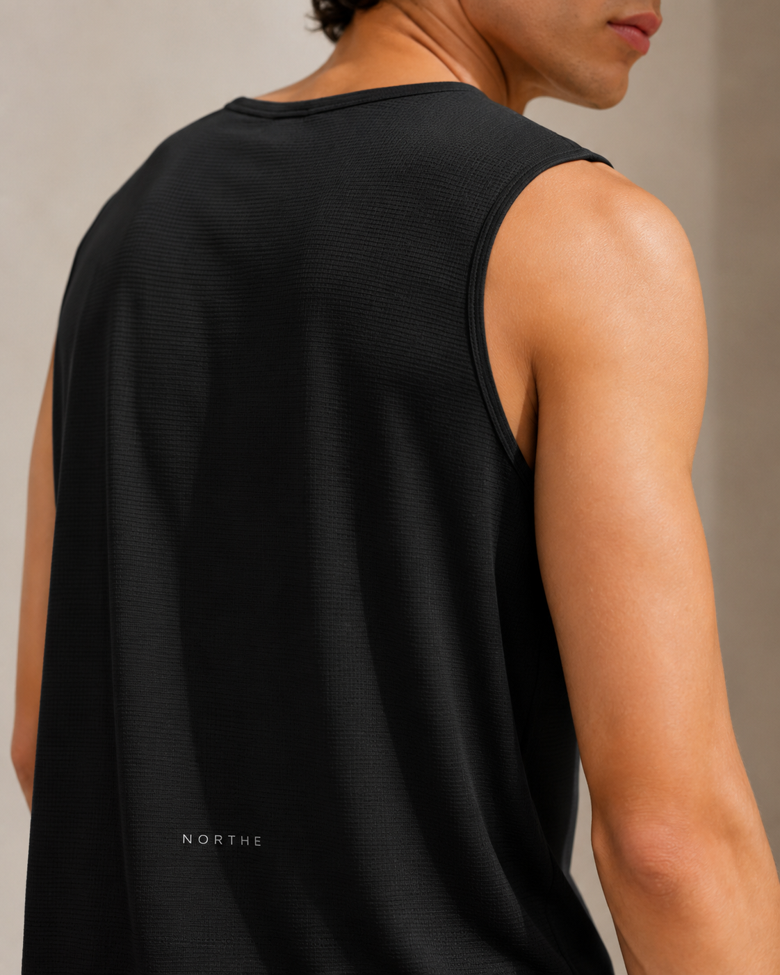 Close-up back view of a man wearing a black ribbed sleeveless tank top with a small white 'NORTHE' logo near the lower left back, against a neutral beige background.
