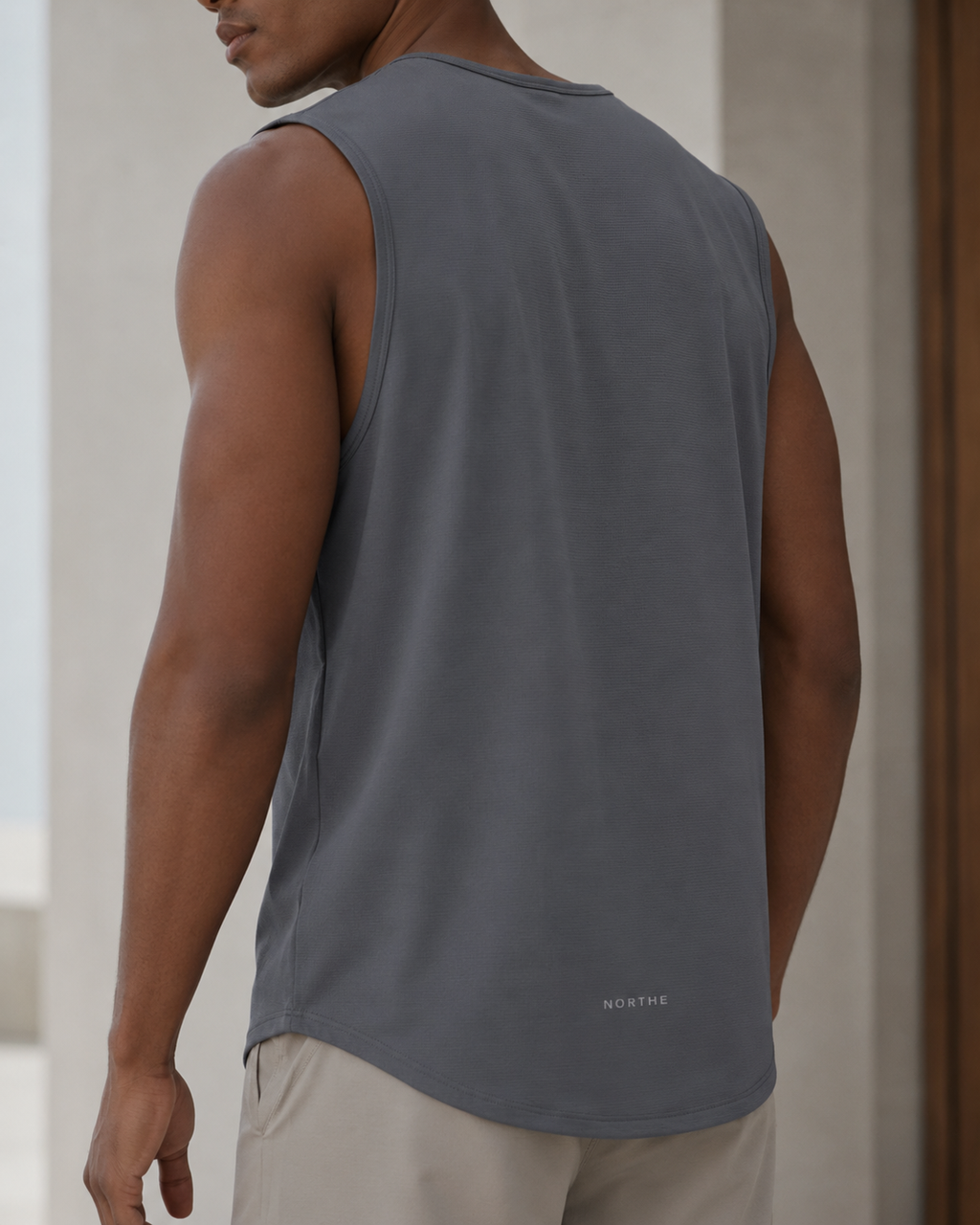 A man wearing a slate gray sleeveless tank top, shown from the back. The tank top has a subtle white 'NORTHE' logo printed near the lower right hem.